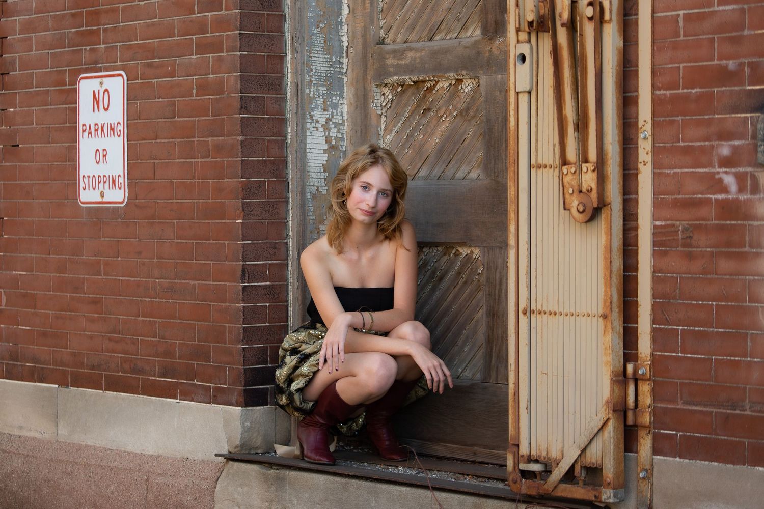 A person in a black dress crouches in a brick doorway during an urban photoshoot.