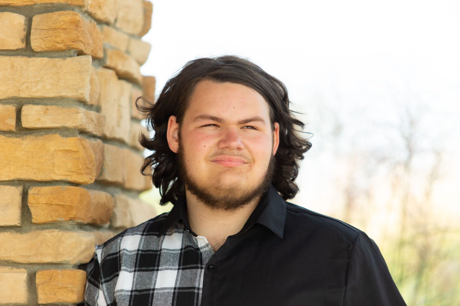 Person in plaid shirt poses against yellow brick wall in outdoor portrait.