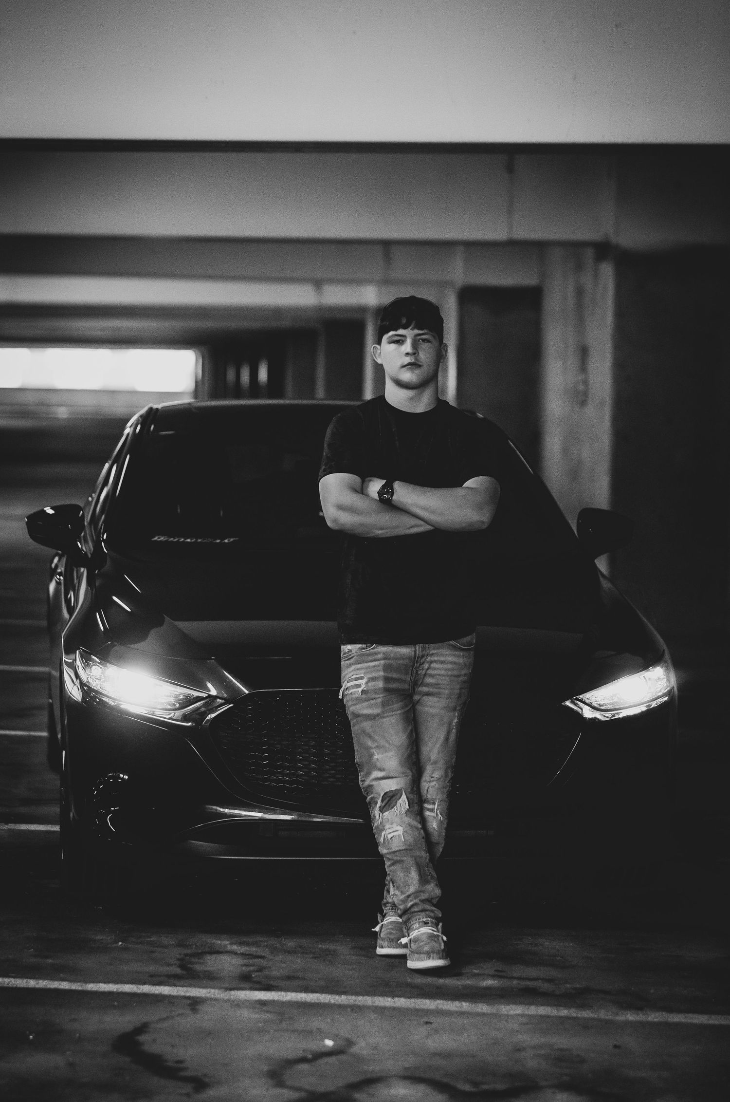 Moody portrait of person leaning against black car in parking garage with headlights on.