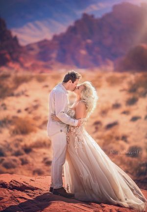 Sunset wedding photo with couple embracing on red rocks with mountain vista.