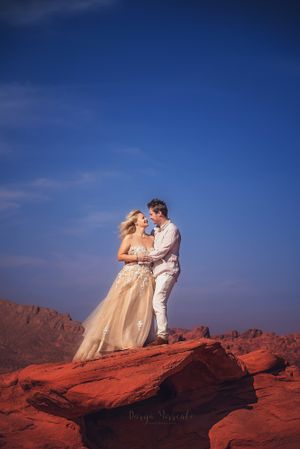 Wedding couple standing on red rocks against deep blue desert sky.