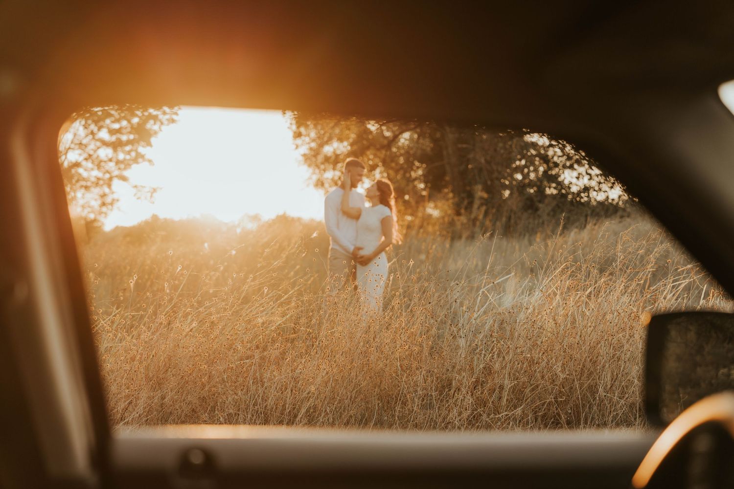 Sunset couples session in Mckinney Texas. Photo of a couple in a field out a car window with sunset behind them.