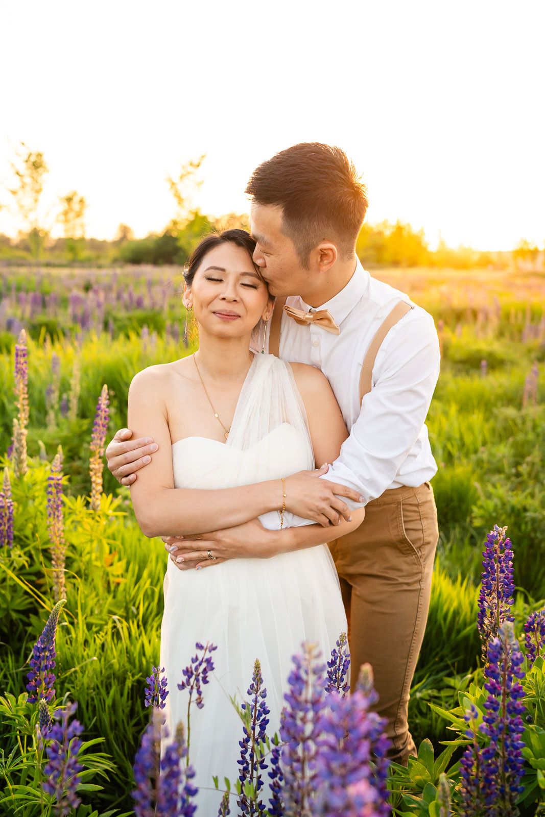 Husband kissing wife at sunset in wildflower lupine field.