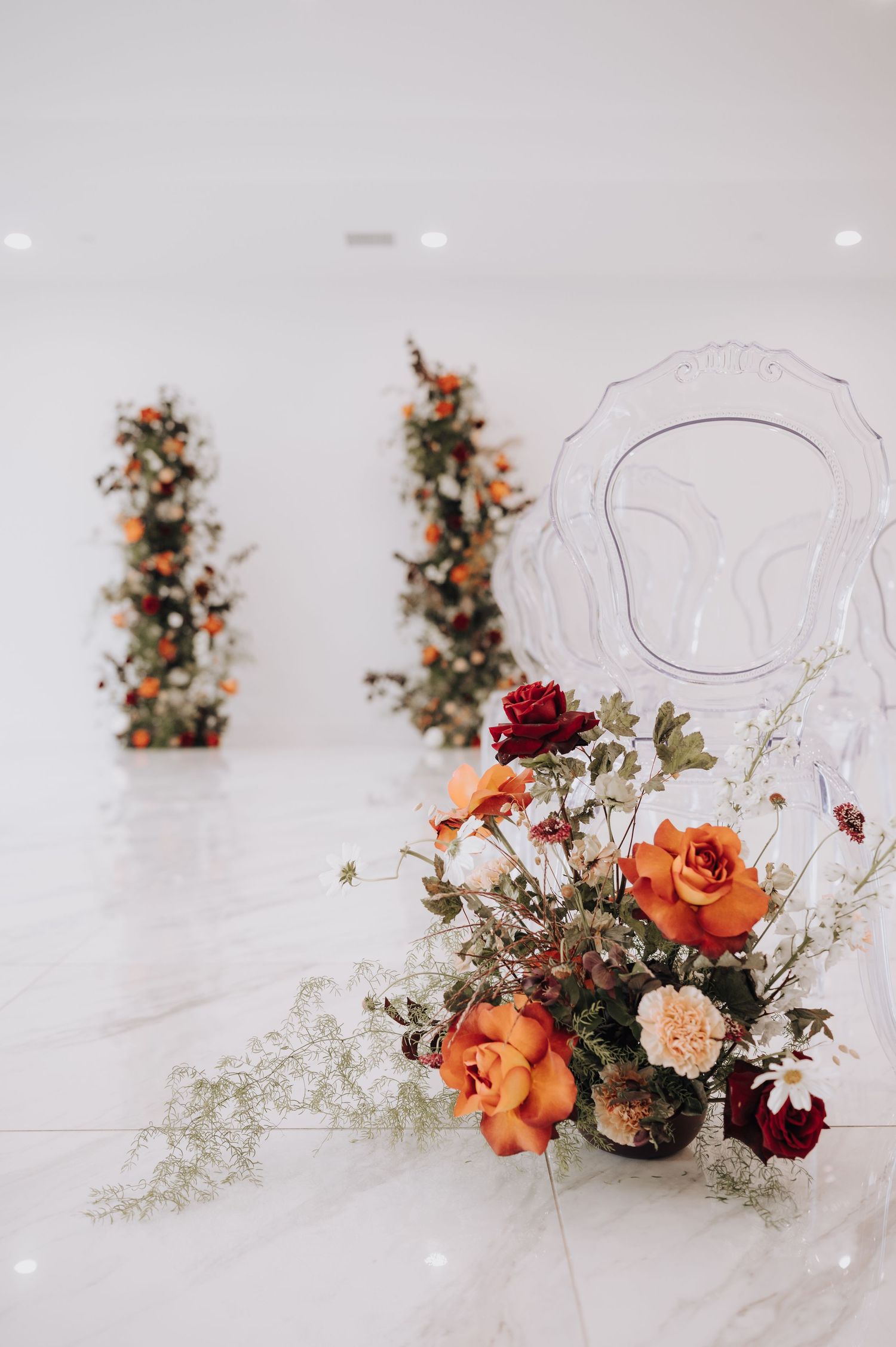 Close-up of vibrant orange and burgundy floral arrangement against white wall.