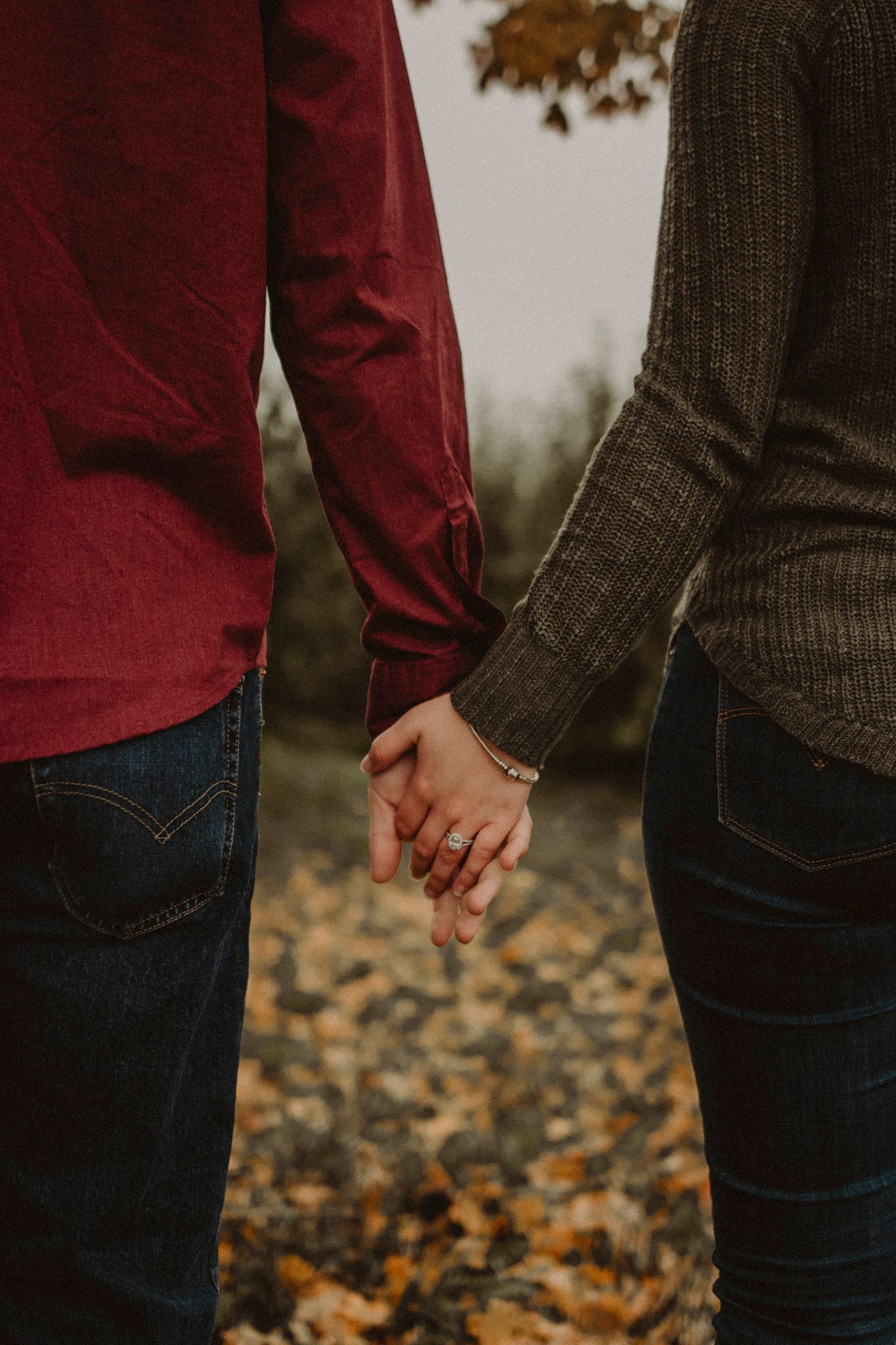 Close-up of couple holding hands while wearing casual fall attire.