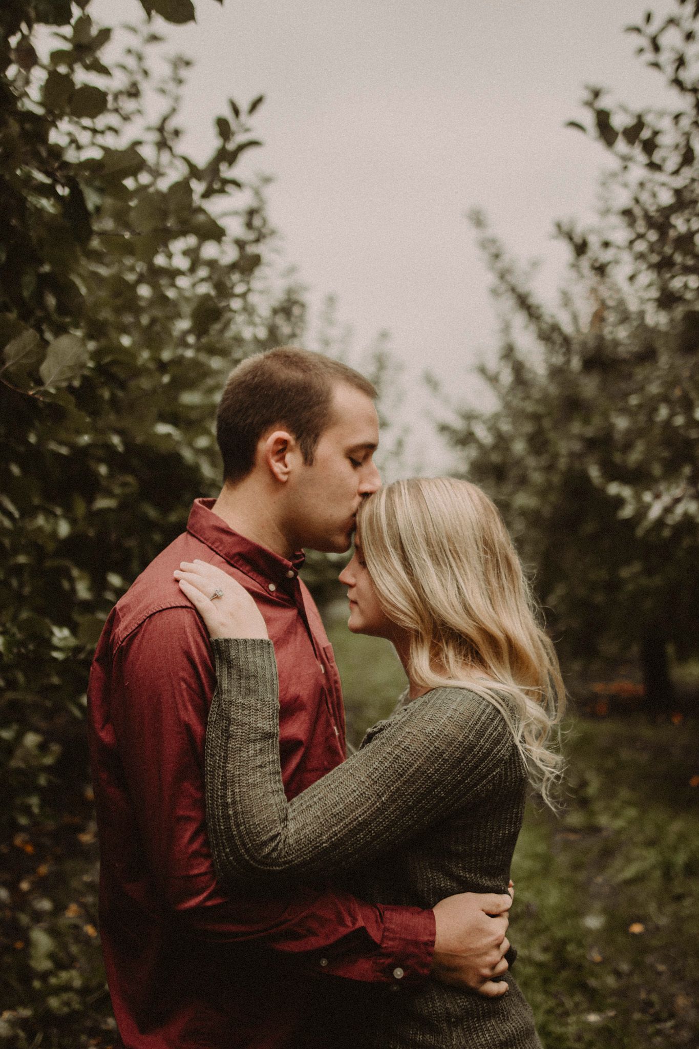 Intimate portrait of couple in casual autumn wear among orchard trees.