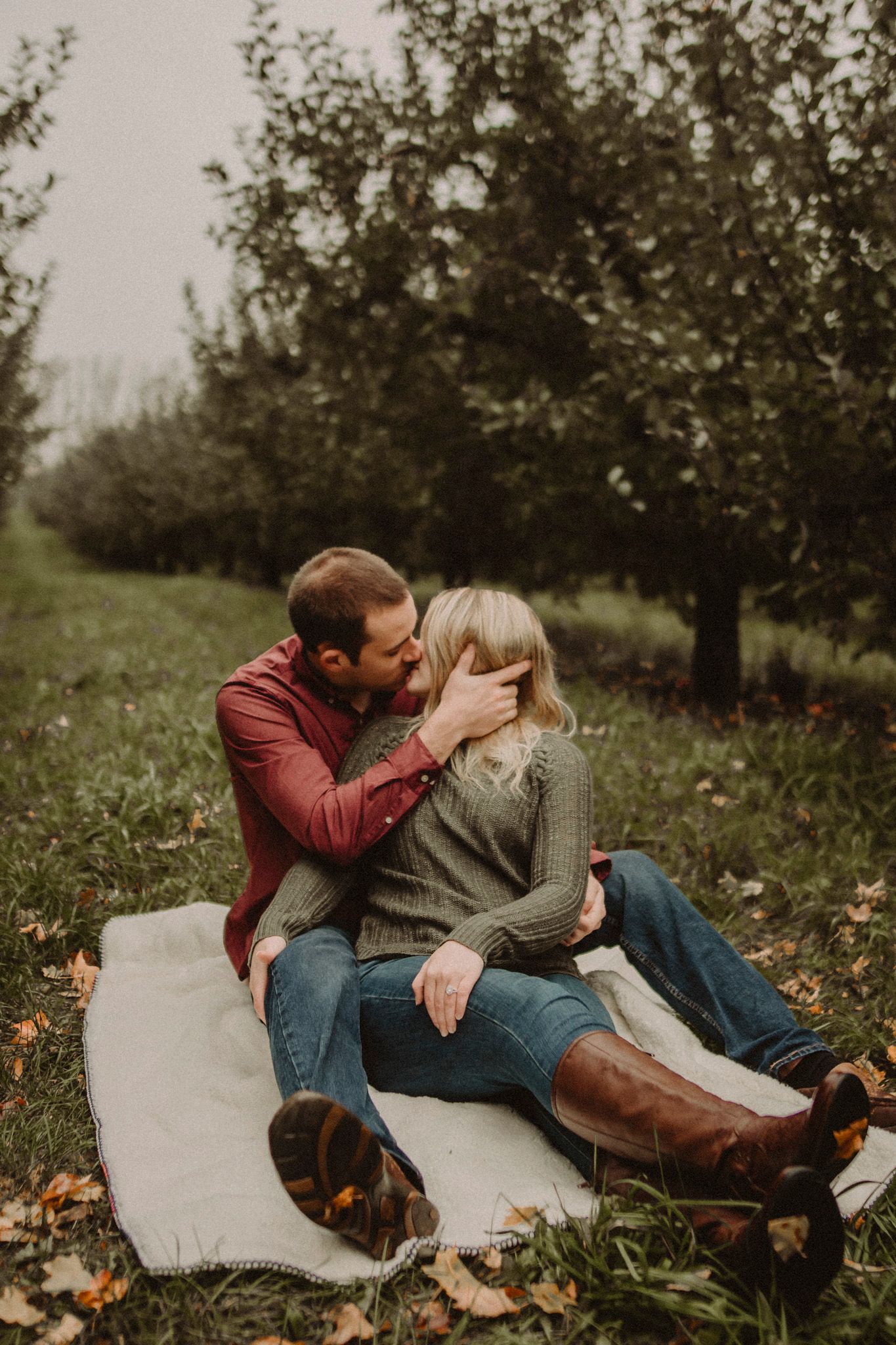 Couple sitting on blanket in orchard during fall photo session.
