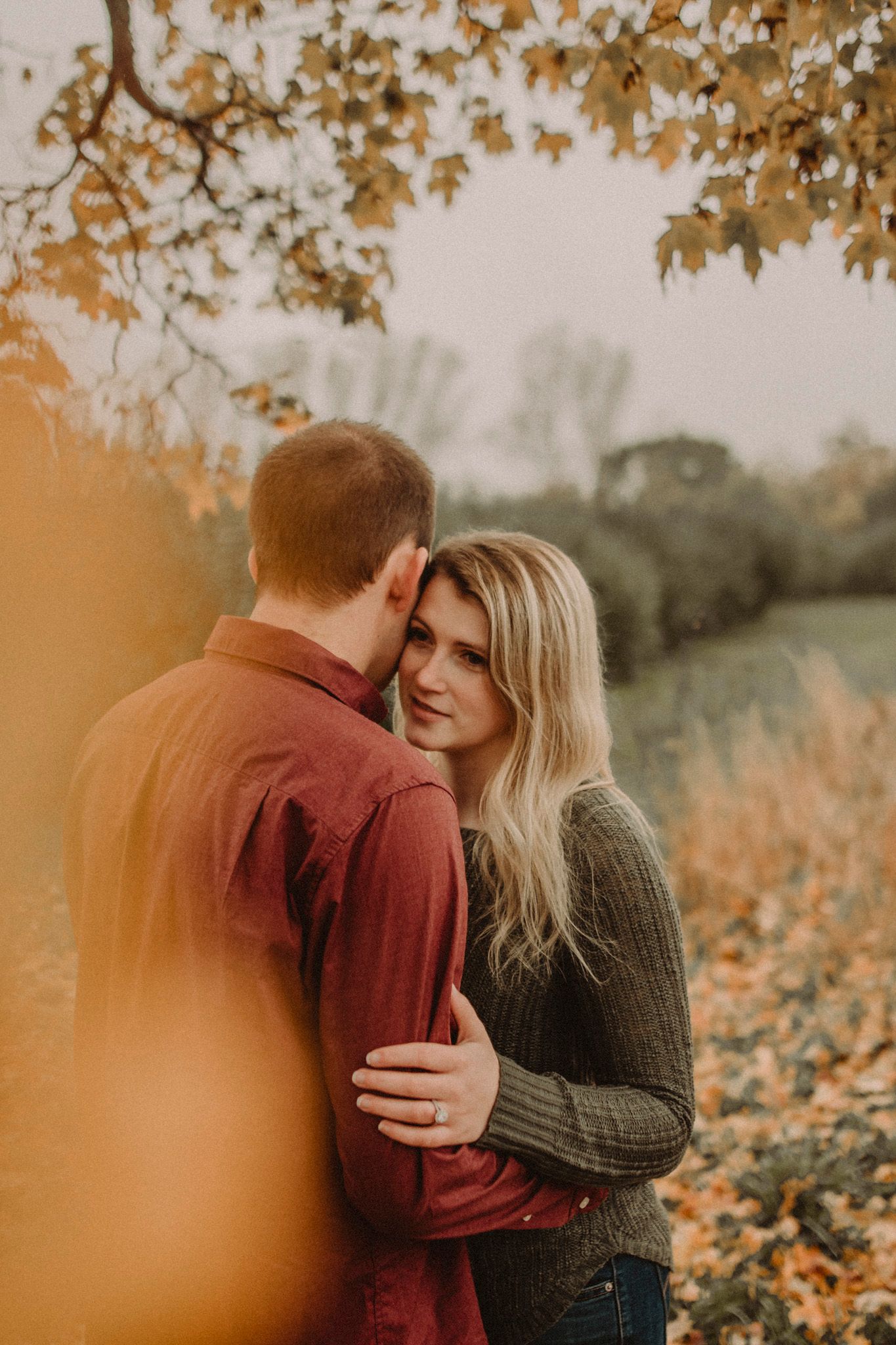 Romantic autumn couple embracing in golden sunlight with fall foliage in background.