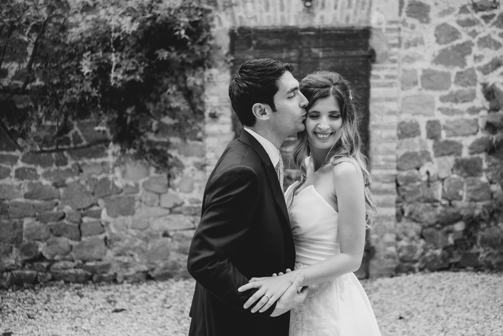 Wedding couple poses against rustic stone wall in black and white photography.