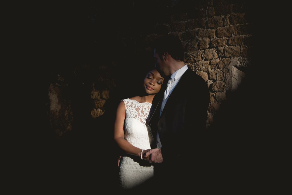 Dramatic low-light portrait of couple against stone wall texture.
