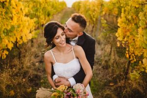 Newlyweds share intimate moments in autumn vineyard with golden foliage backdrop.