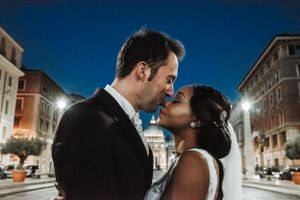 Nighttime wedding portrait with illuminated city buildings in background.