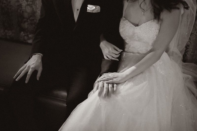 Black and white detail photo of couple's hands on wedding dress.