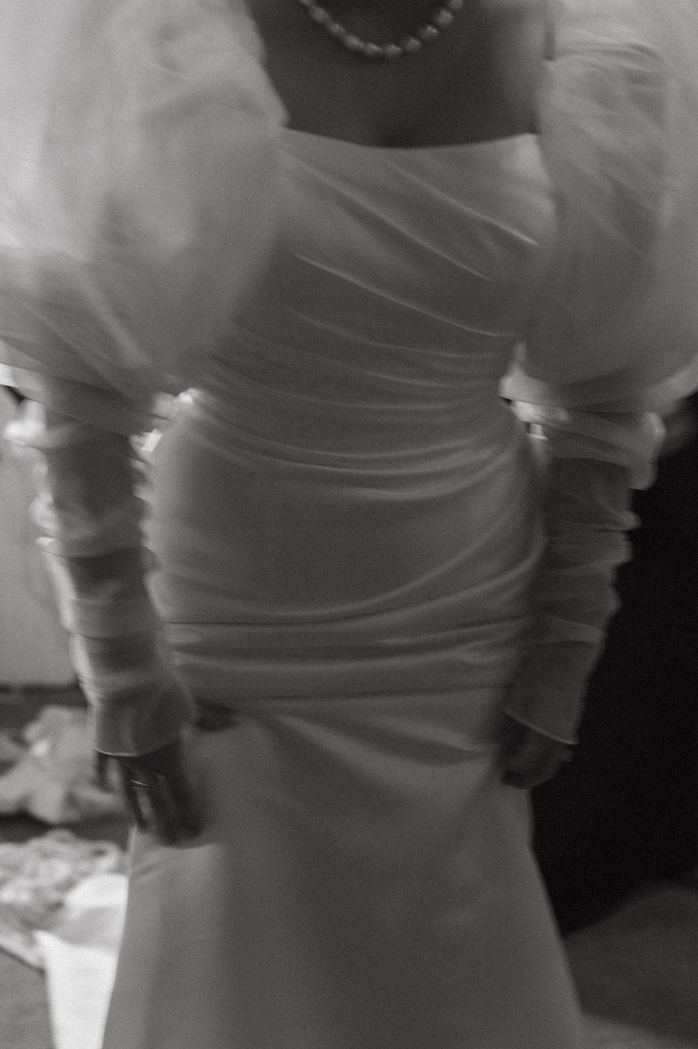 Close-up detail of a white wedding dress showing ruched fabric and sheer sleeves.