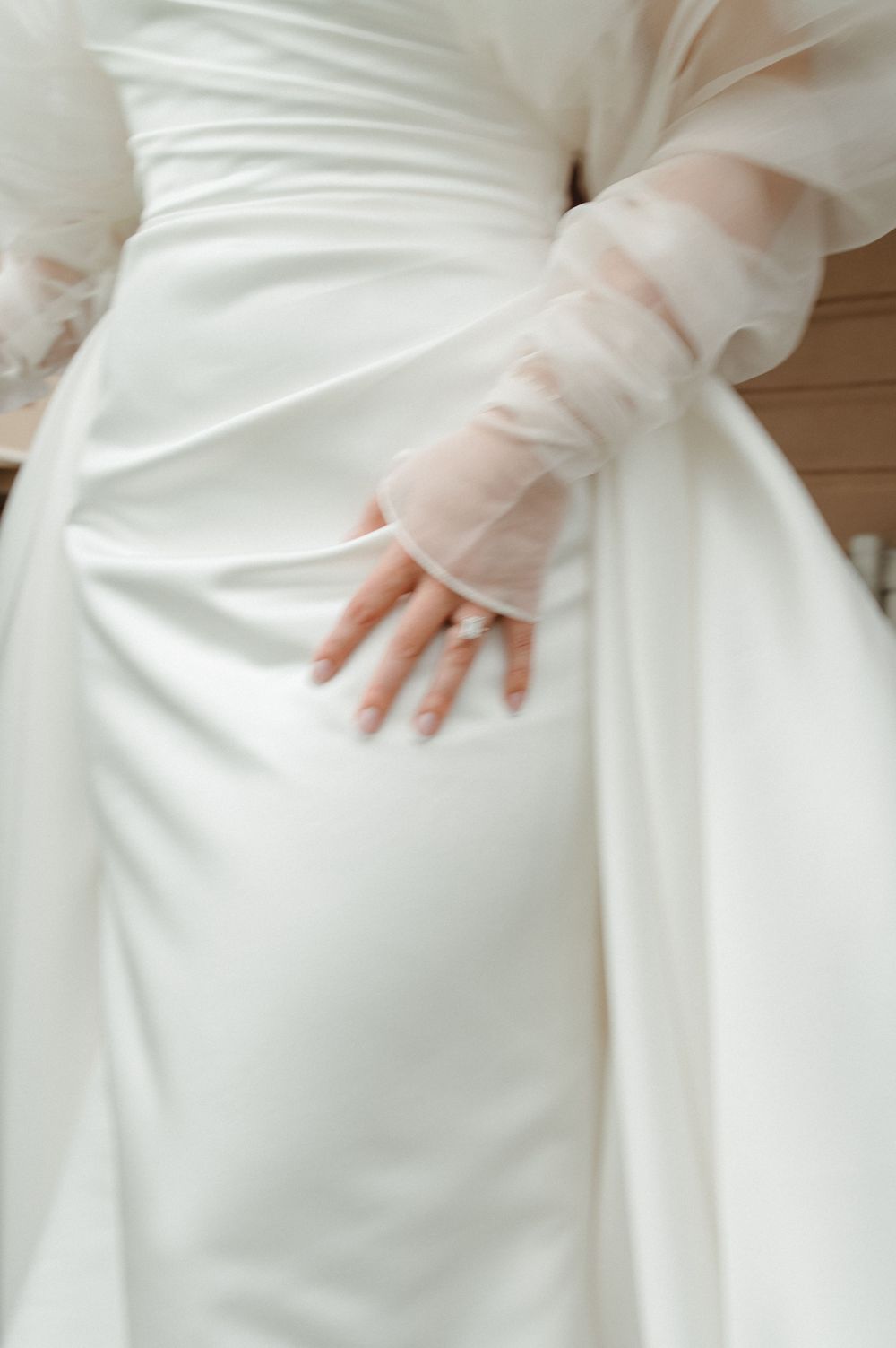 Detailed view of a white wedding dress with sheer sleeves and delicate fabric draping.