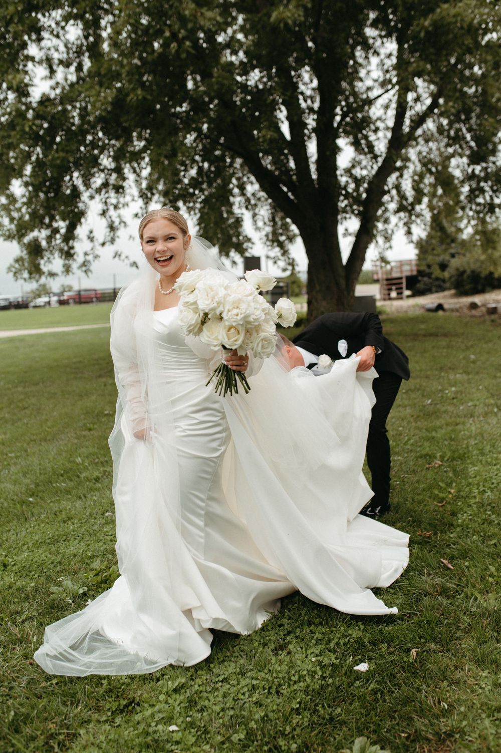 A joyful bride in a white wedding dress holding a bouquet of white flowers outdoors.