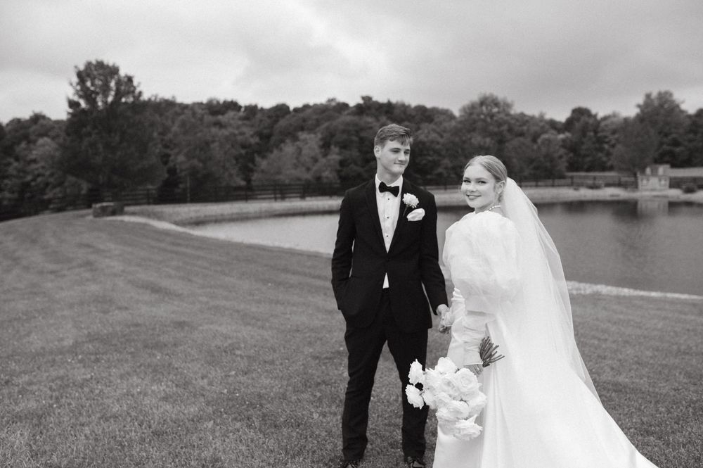 Elegant black and white wedding portrait of a couple standing by a lake.