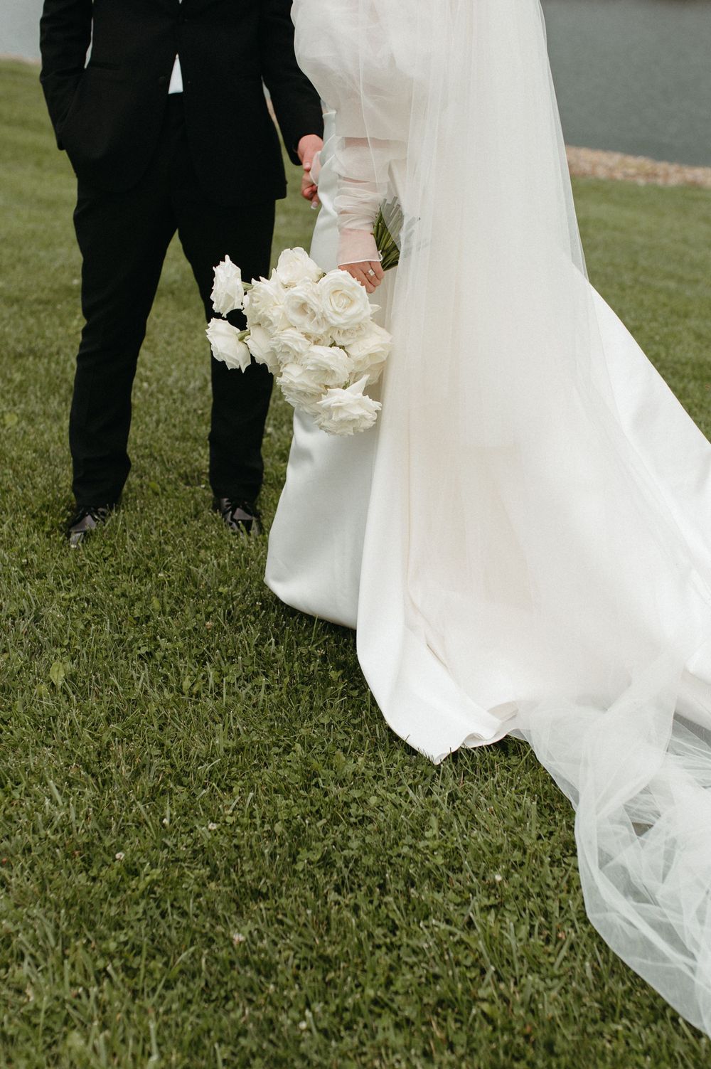 Close-up of wedding dress train and white rose bouquet against green grass.