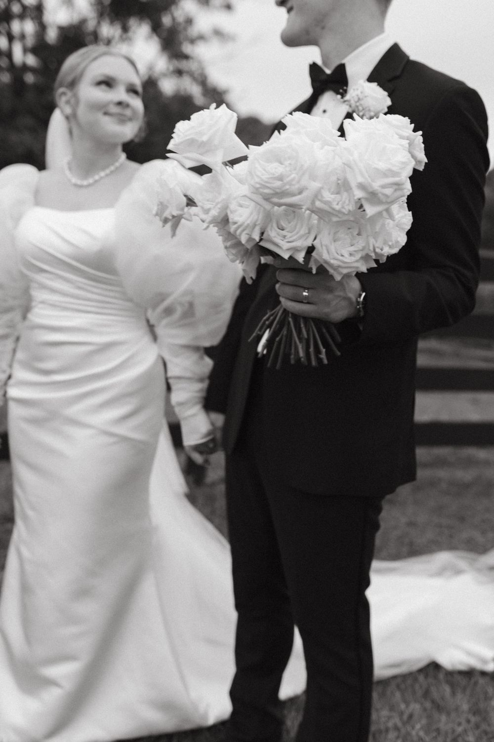 Black and white photo of couple with large white rose bouquet at their wedding.