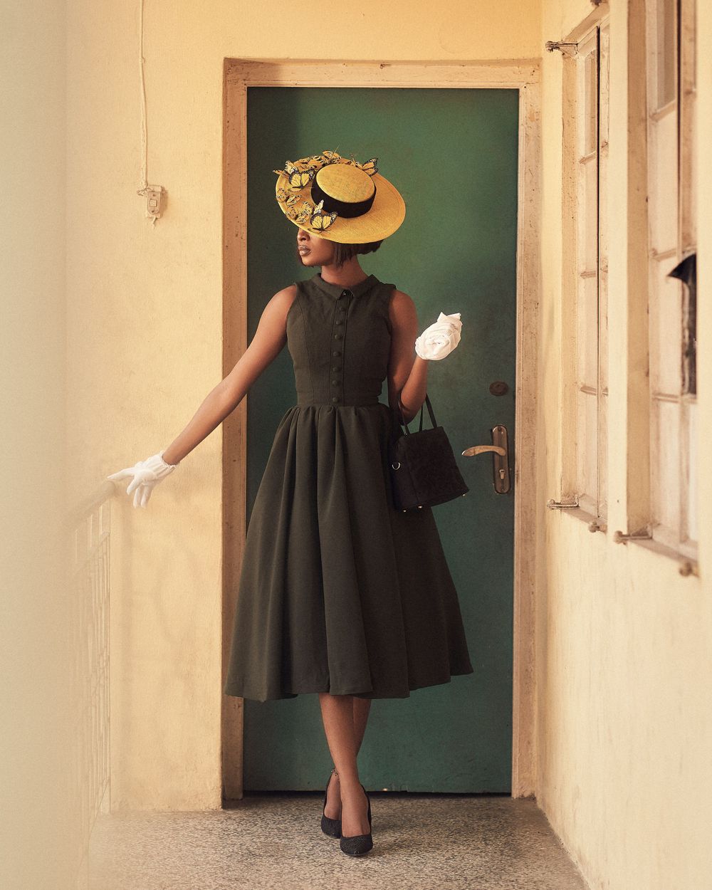 A stylish vintage-inspired pose in a dark dress and decorative hat against a green door.