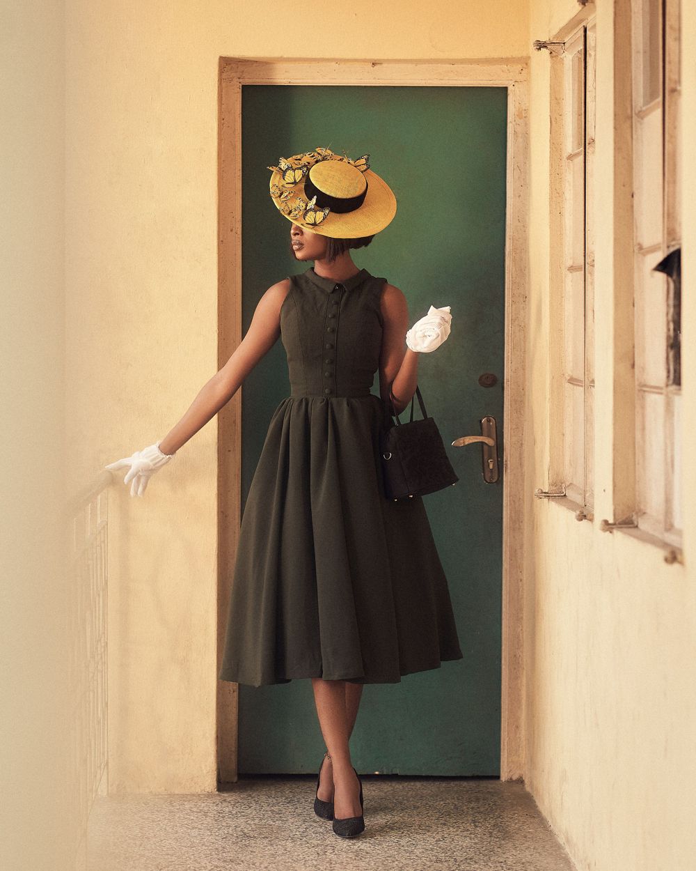 A vintage-inspired outfit featuring a dark dress and decorative hat posed in a doorway.