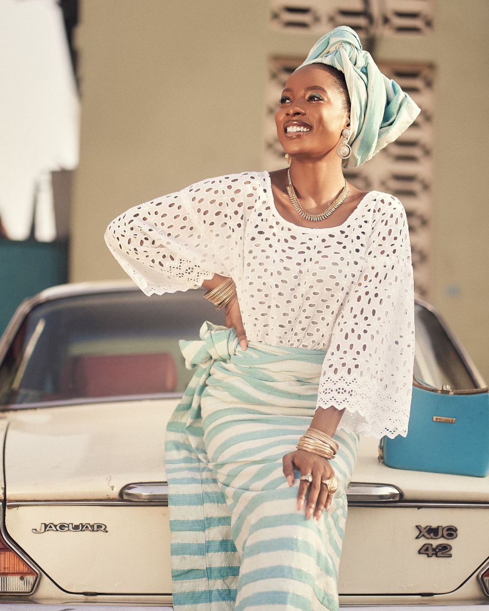 Joyful pose in white crochet sweater and striped skirt next to vintage car.