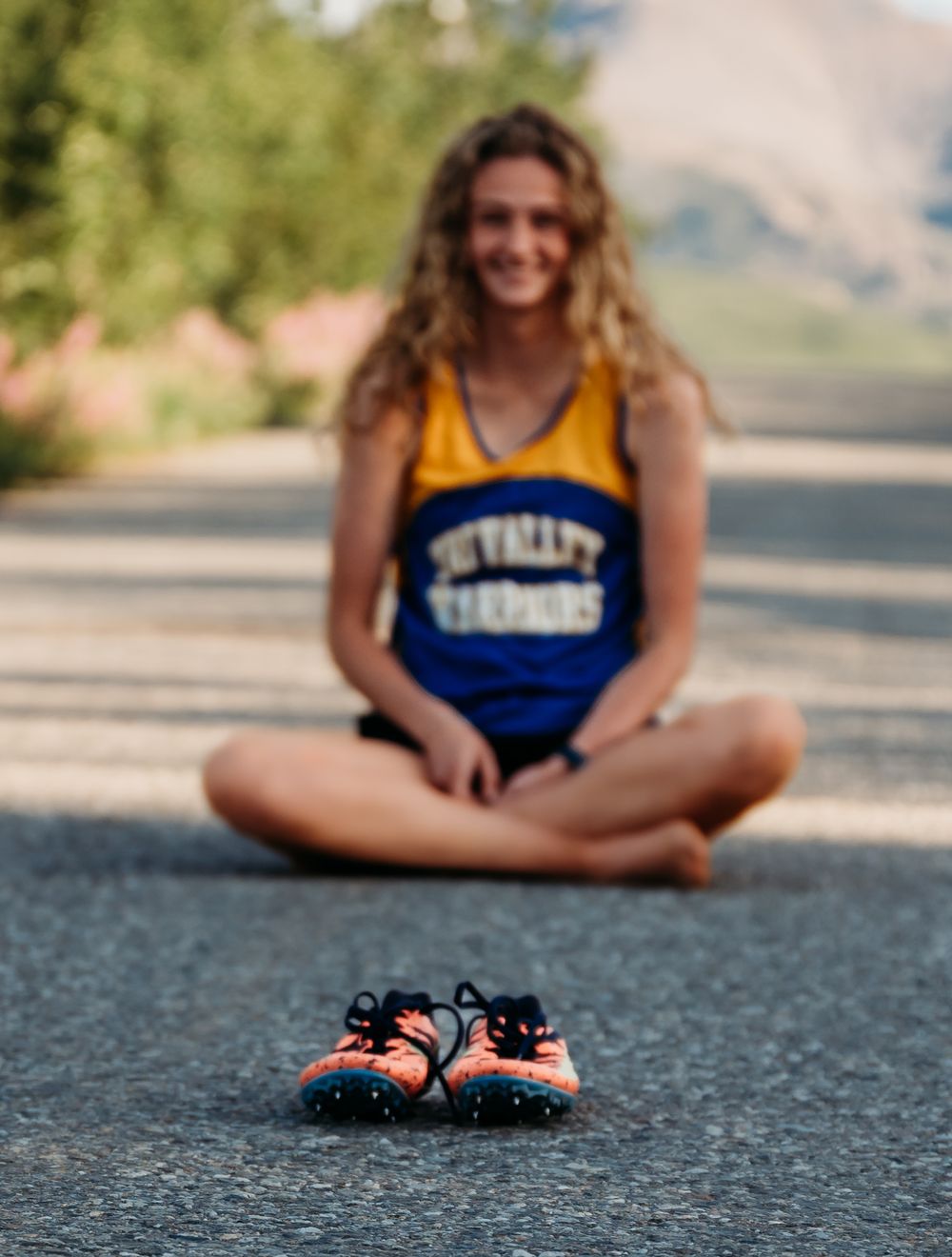 Athlete in yellow and blue uniform sitting cross-legged with shoes placed in front.