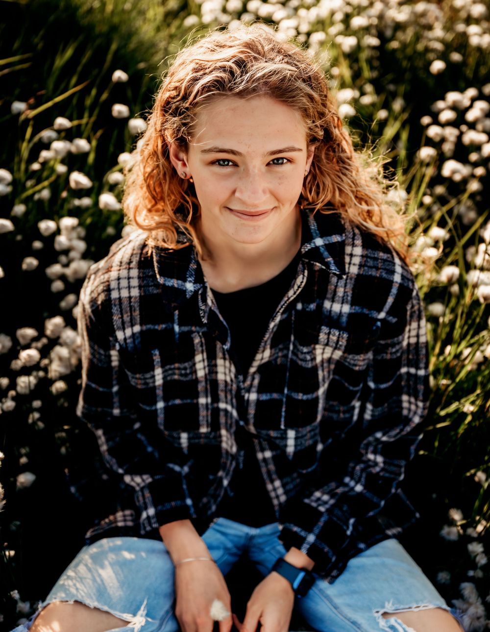 Portrait of someone wearing plaid flannel shirt sitting outdoors among white flowers.