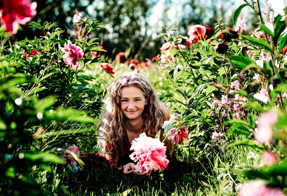 Someone peeking through lush garden foliage surrounded by blooming pink flowers.