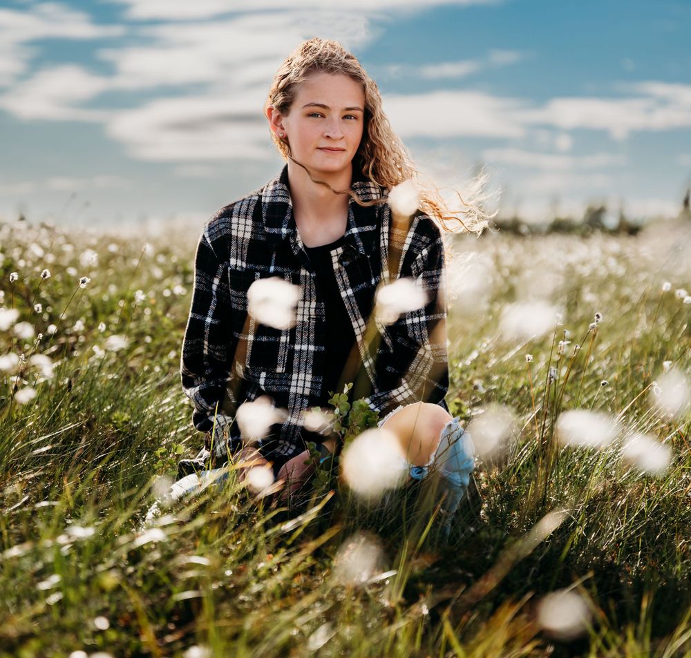 Person sitting in field of white wildflowers under cloudy blue sky.
