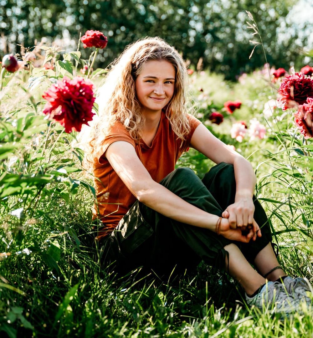 Person in rust-colored shirt sitting among blooming red flowers in garden.