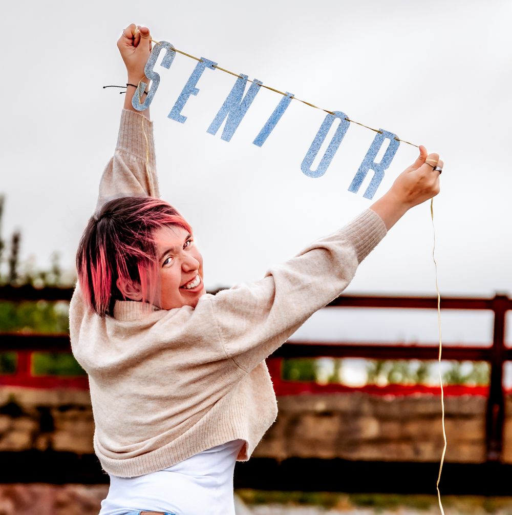 Person in beige sweater holding up decorative text banner outdoors.