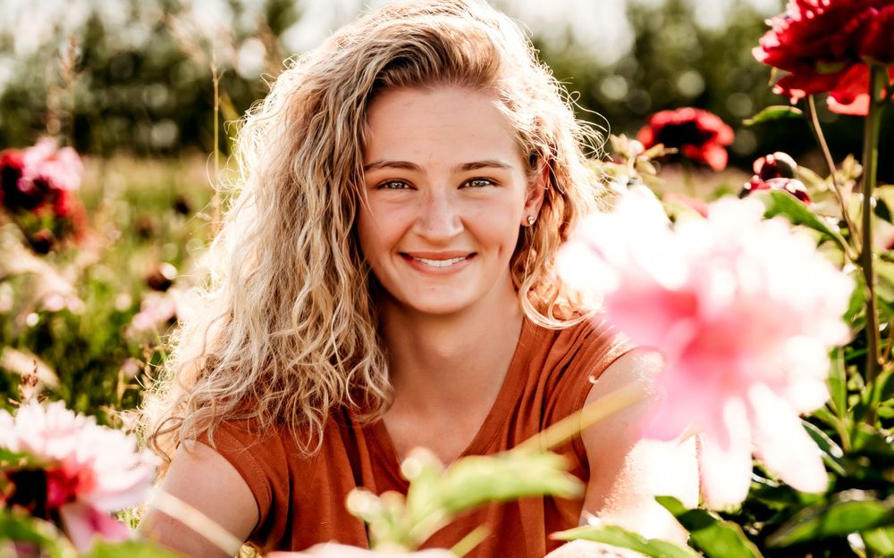 A joyful moment captured in a garden filled with vibrant pink and red flowers on a sunny day.