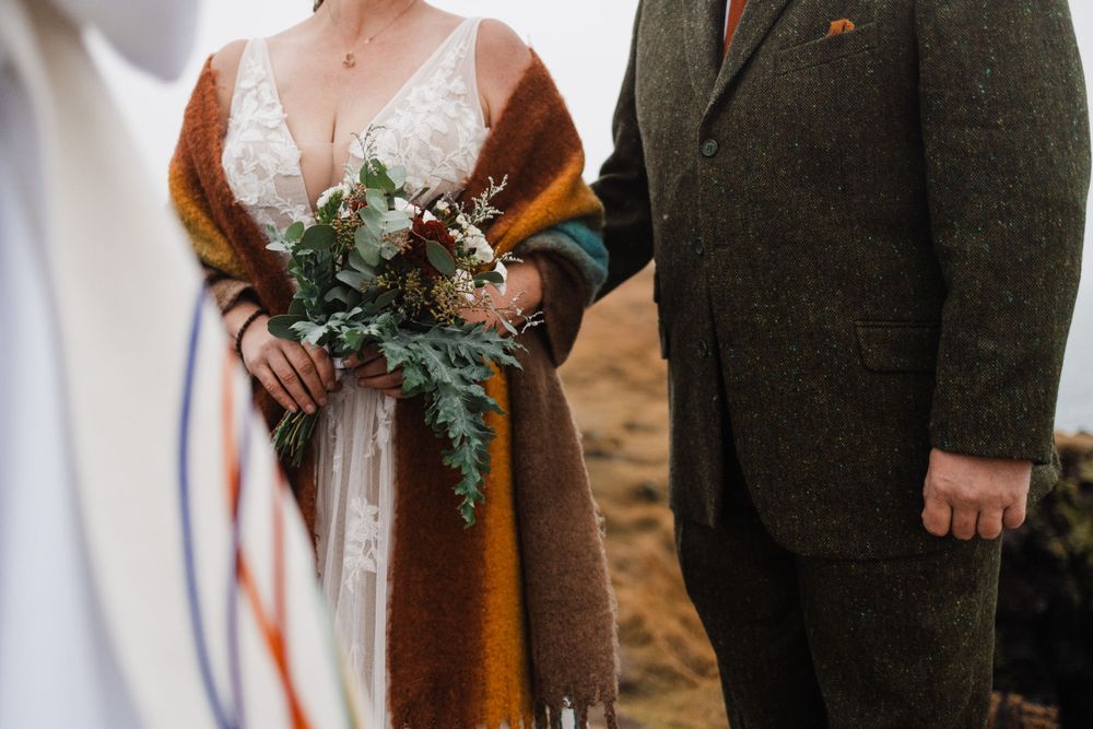 Wedding ceremony details showing tweed suit and bridal bouquet with orange wrap.