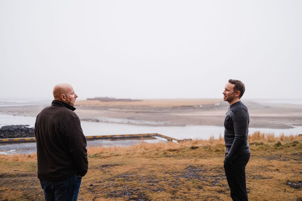 Two people having conversation on coastal clifftop with water views.