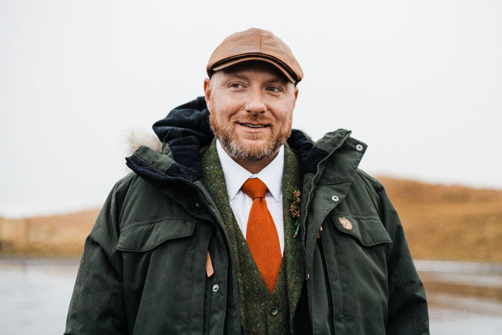 Winter wedding attire with orange tie and dark coat against coastal landscape.