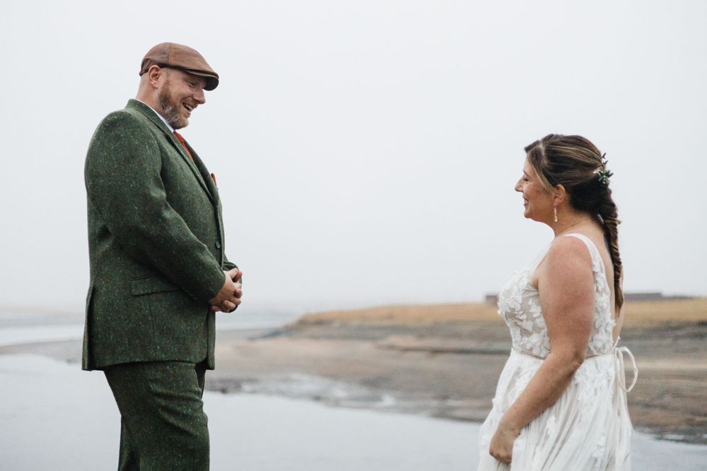 A wedding couple stands face to face on a coastal cliff in moody weather.
