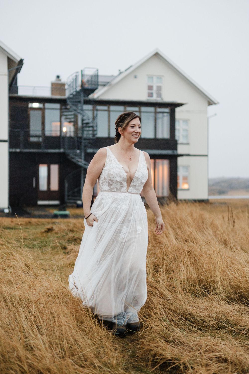 A white wedding dress flows in the wind against tall grass and modern coastal architecture.