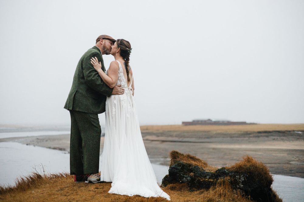 A couple shares an intimate moment on a misty cliff overlooking a coastal landscape.