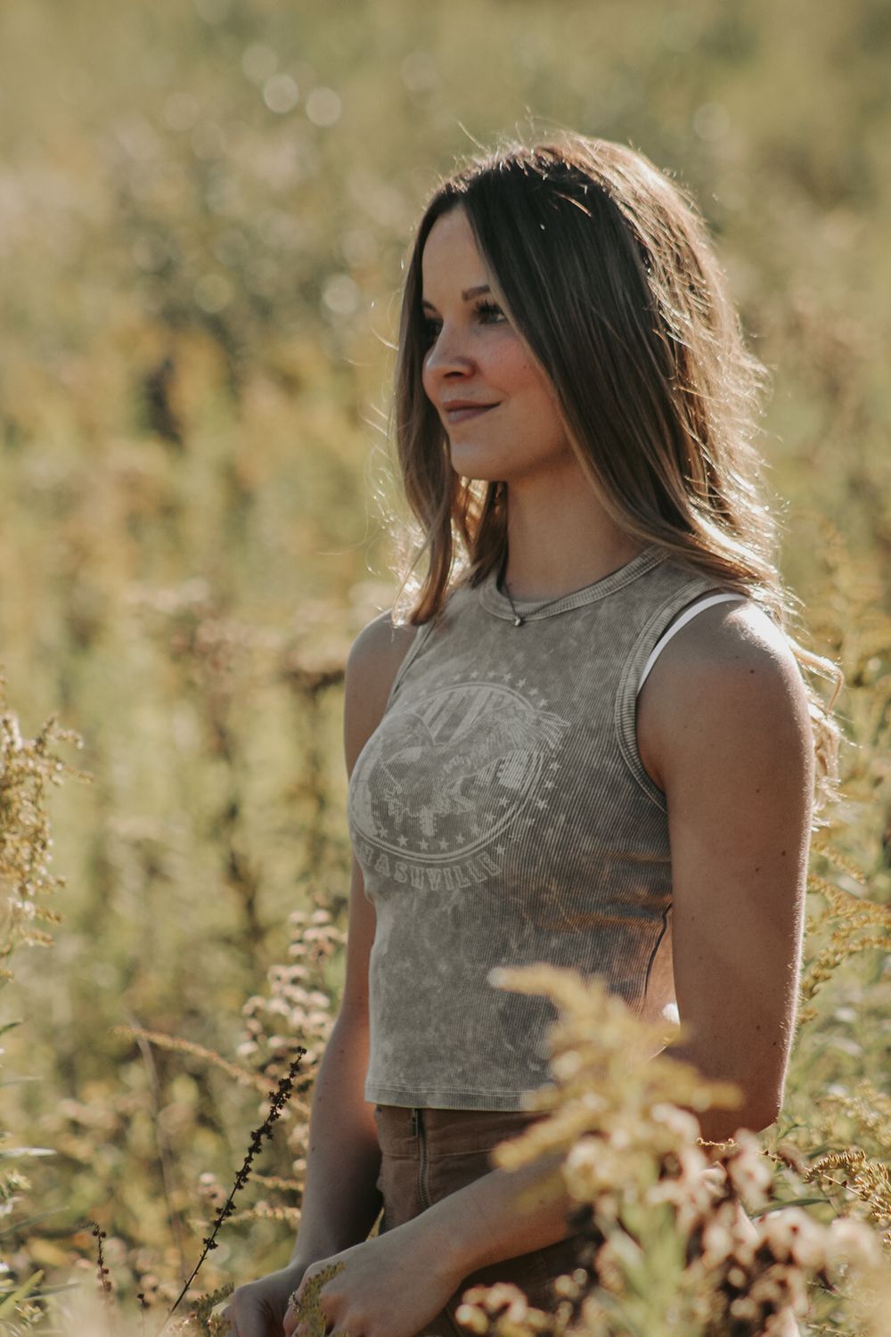Portrait in grey crop top amid golden wildflowers at sunset.