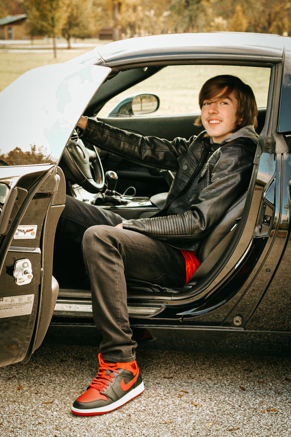 Someone sitting in the driver's seat of a black sports car wearing red sneakers.