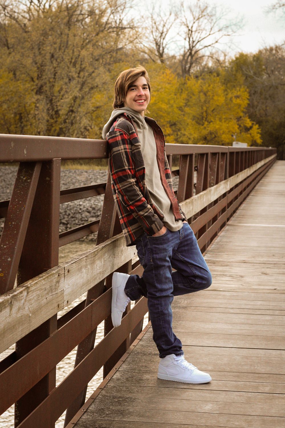 A casual portrait on a wooden bridge with fall foliage in the background.