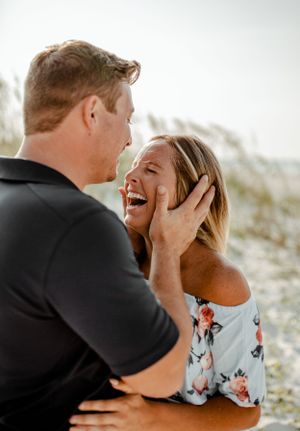 A joyful couple laughing together against a backdrop of coastal dunes.