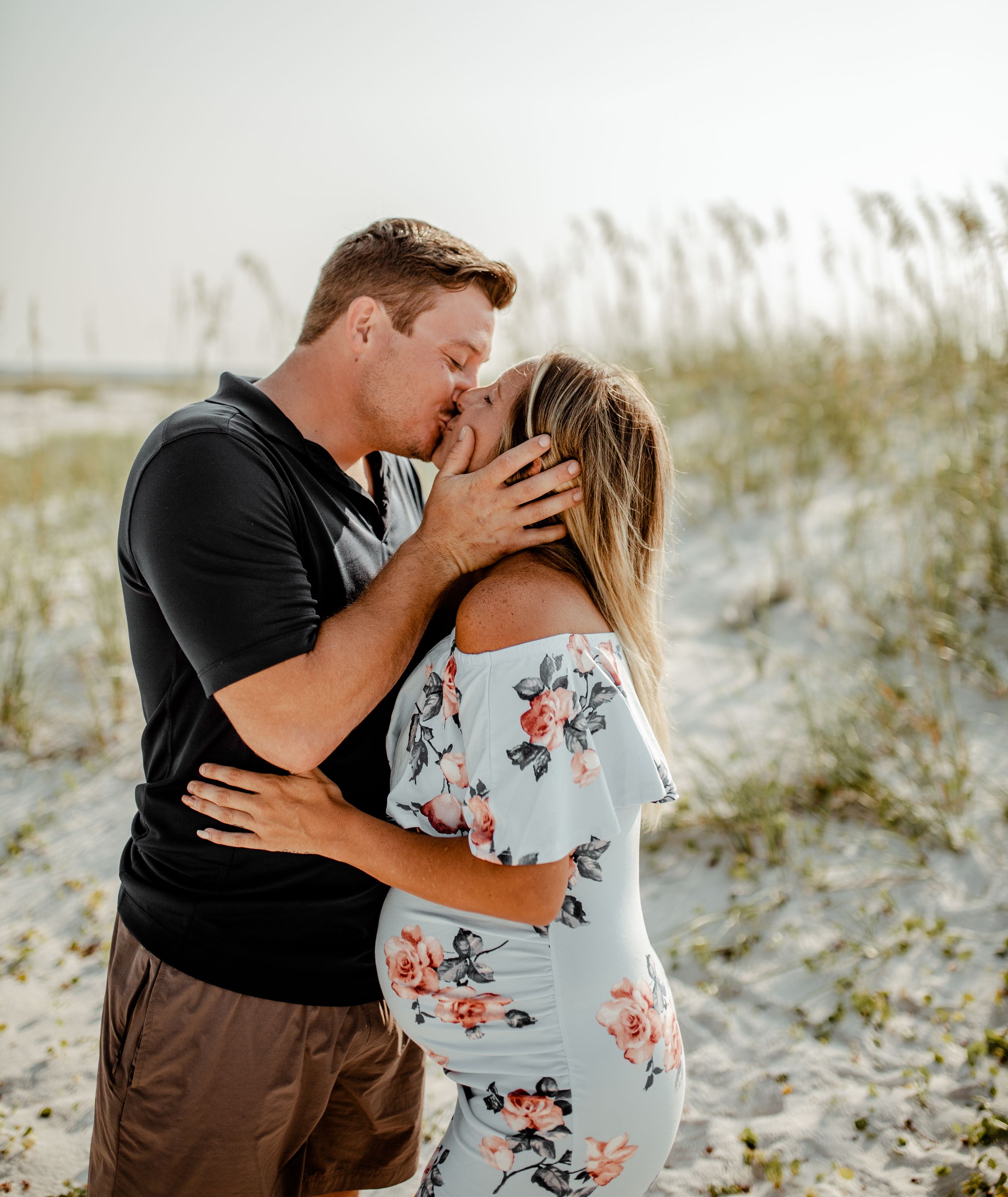A romantic moment captured between a couple on sandy dunes with sea grass.