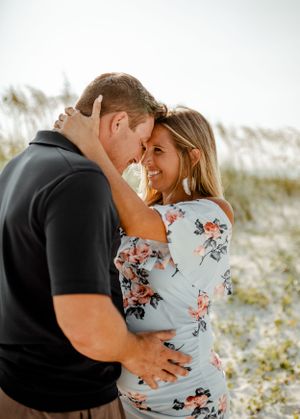 An intimate moment between a couple sharing a tender embrace on a beach with coastal vegetation.