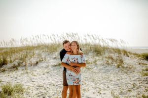 A romantic moment captured between a couple embracing on sand dunes with sea grass in the background.