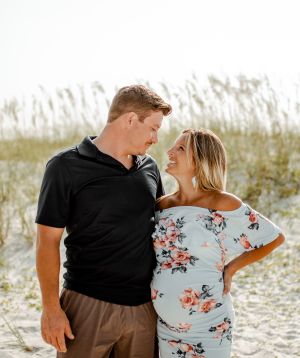 A couple shares a playful moment on a beach with sand dunes and sea oats in the background.