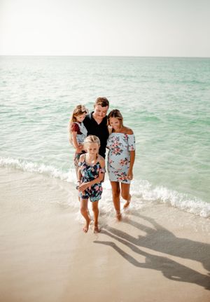 A family of four walks together along the turquoise waters of a beach at sunset.