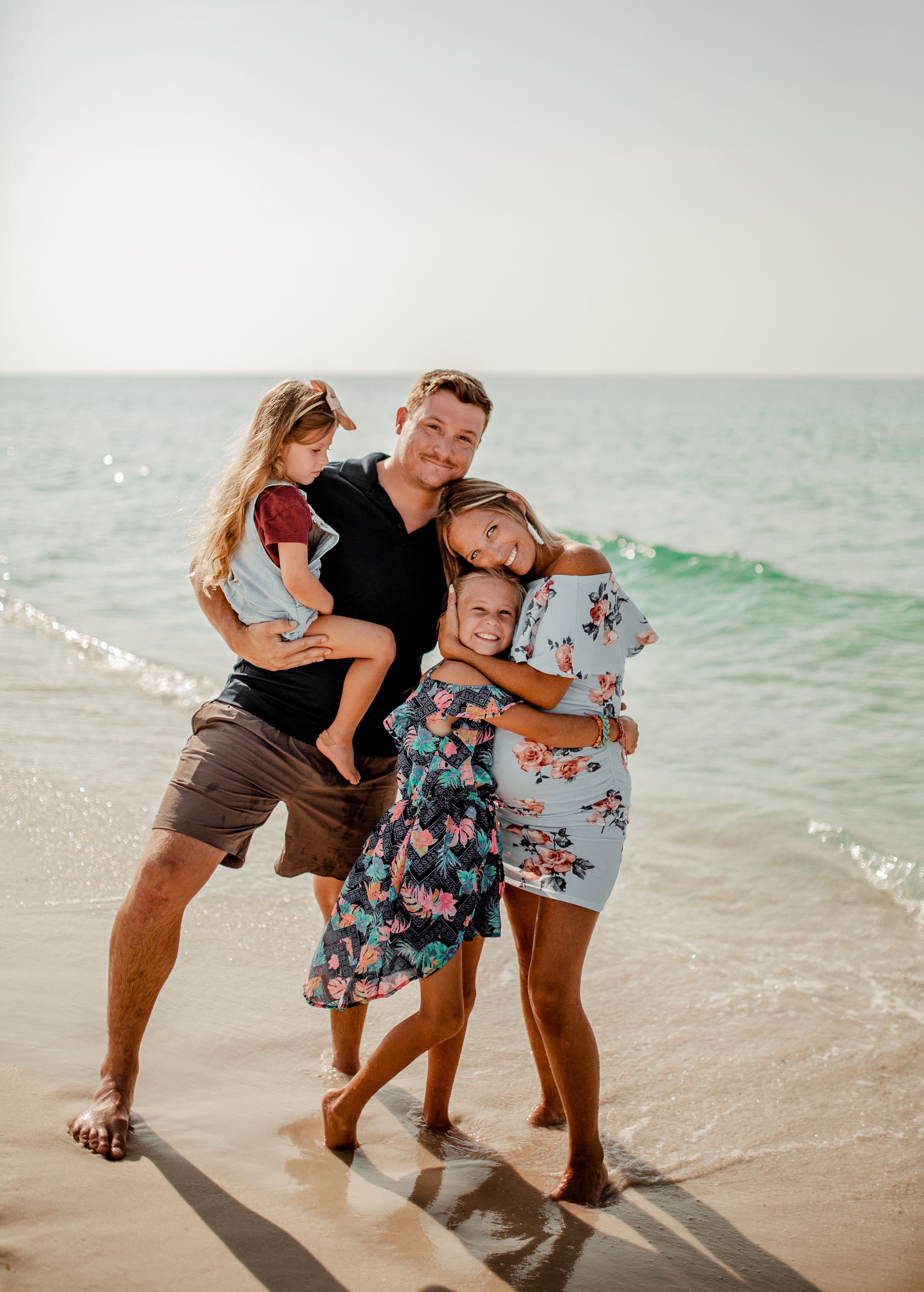A family sharing a group hug on a sunny beach with gentle waves in the background.