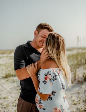 A couple sharing laughter during their beach engagement photoshoot among sand dunes.